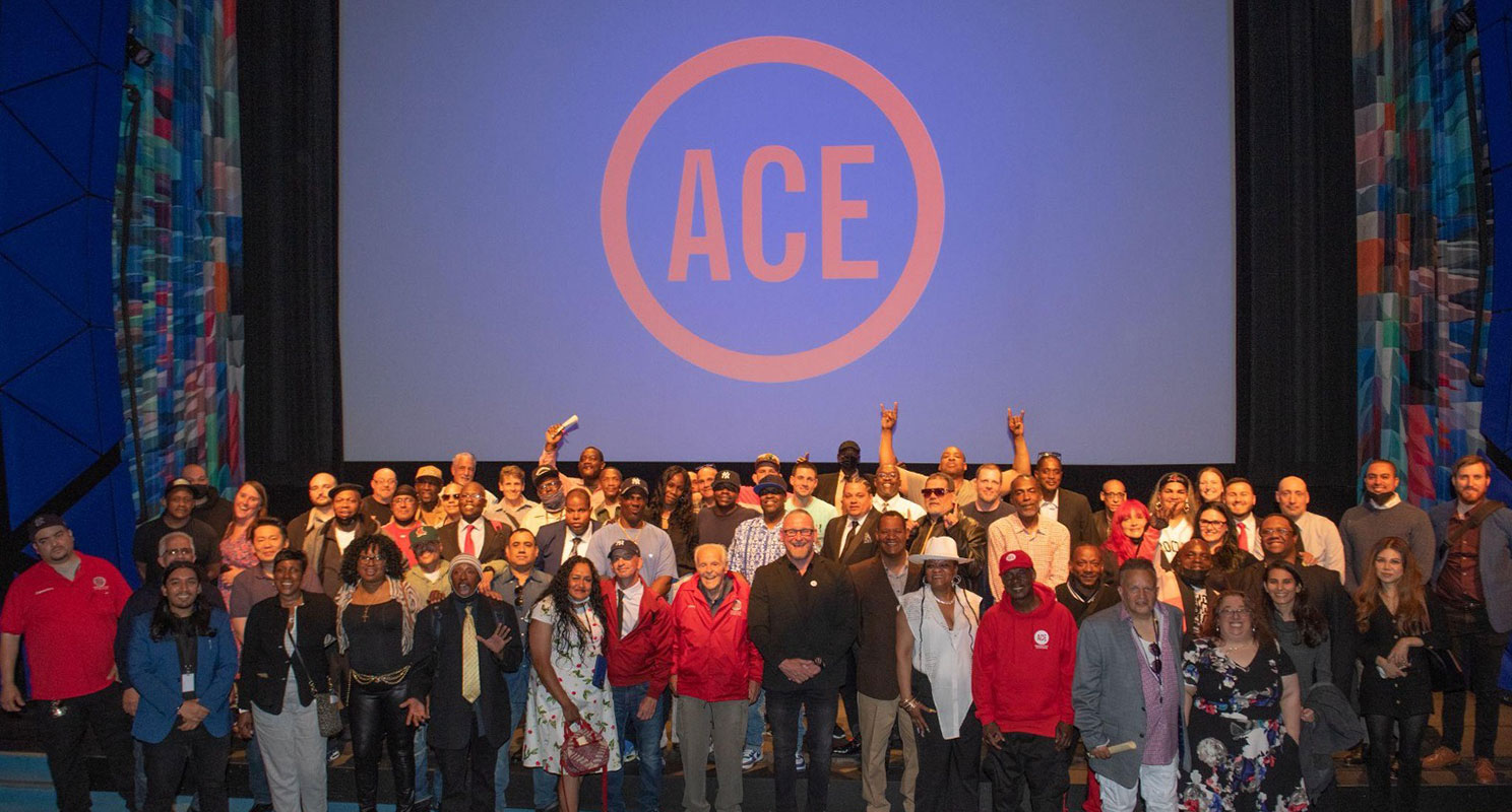 Group of people standing in front of large screen with ACE logo